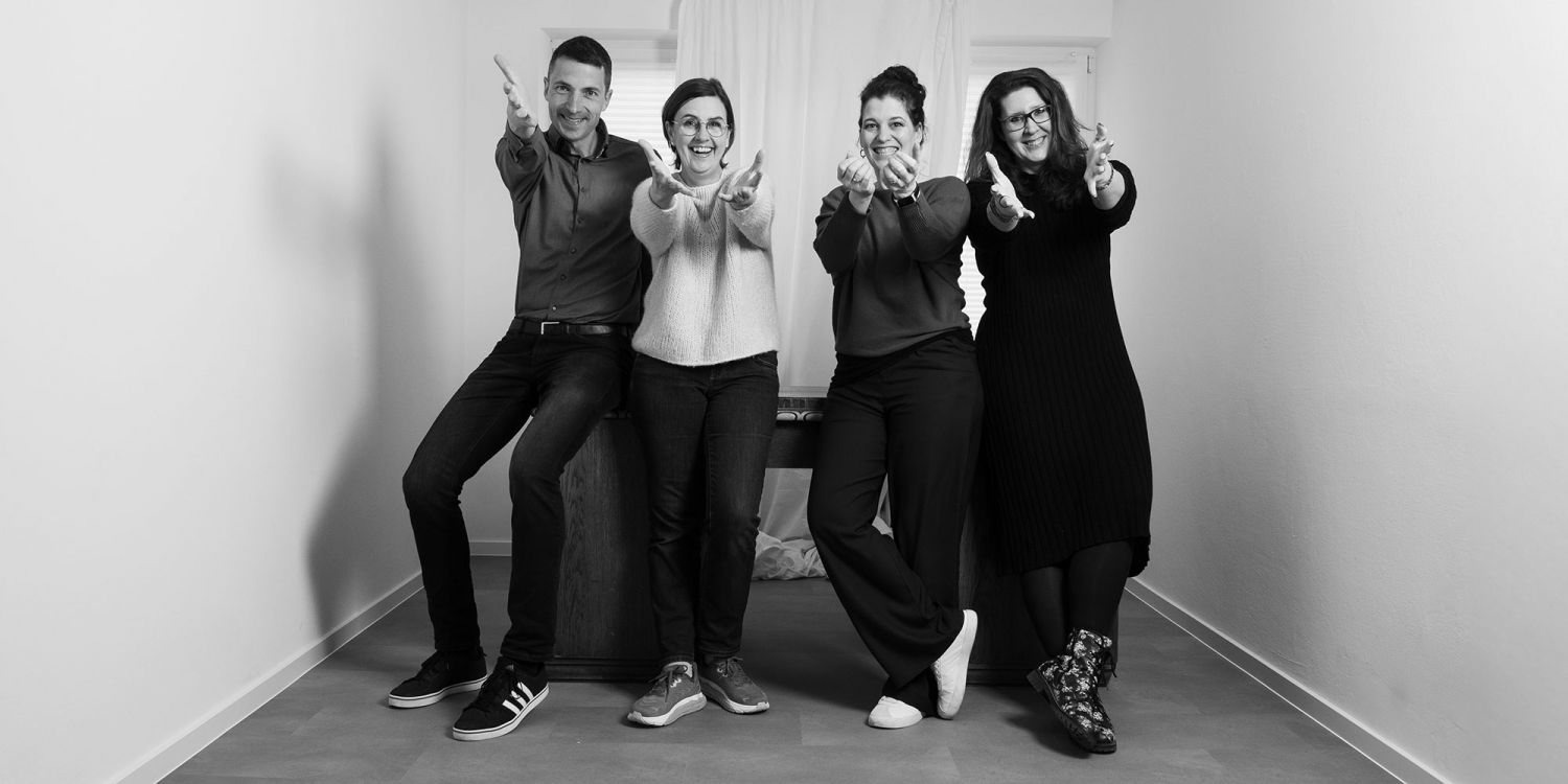 Gruppenfoto der Sichtbar-Macher. Alle lehnen an einem Tisch und strecken die Hände grüßend nach vorn.