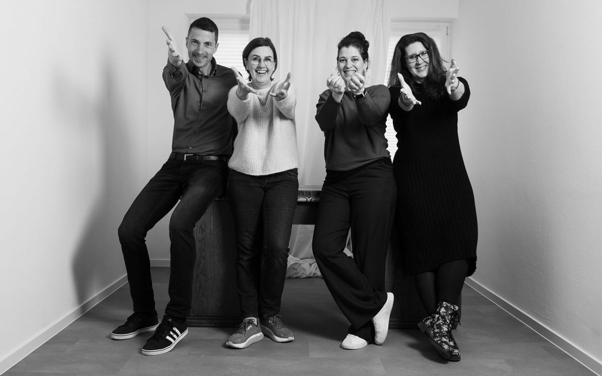 Gruppenfoto der Sichtbar-Macher. Alle lehnen an einem Tisch und strecken die Hände grüßend nach vorn.